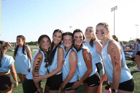 Members of the senior powder puff team smiling on the sidelines and showing off their spirit wear.