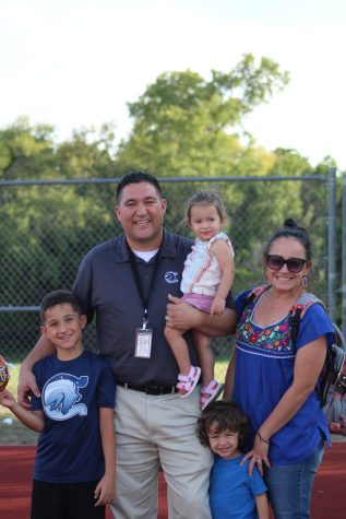 Dr. Beto Hinojosa poses with his wife and children on the Champion football field during a JV football game.